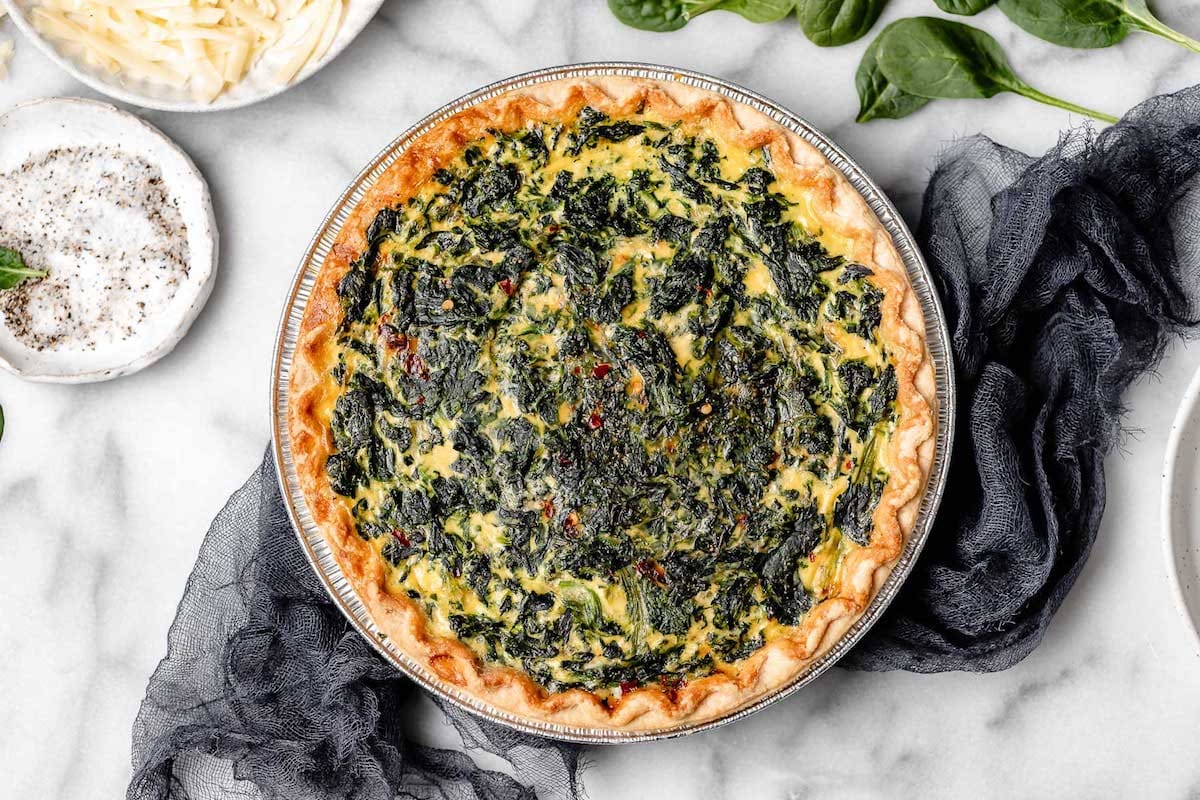 baked spinach quiche in pan with tea towel. 