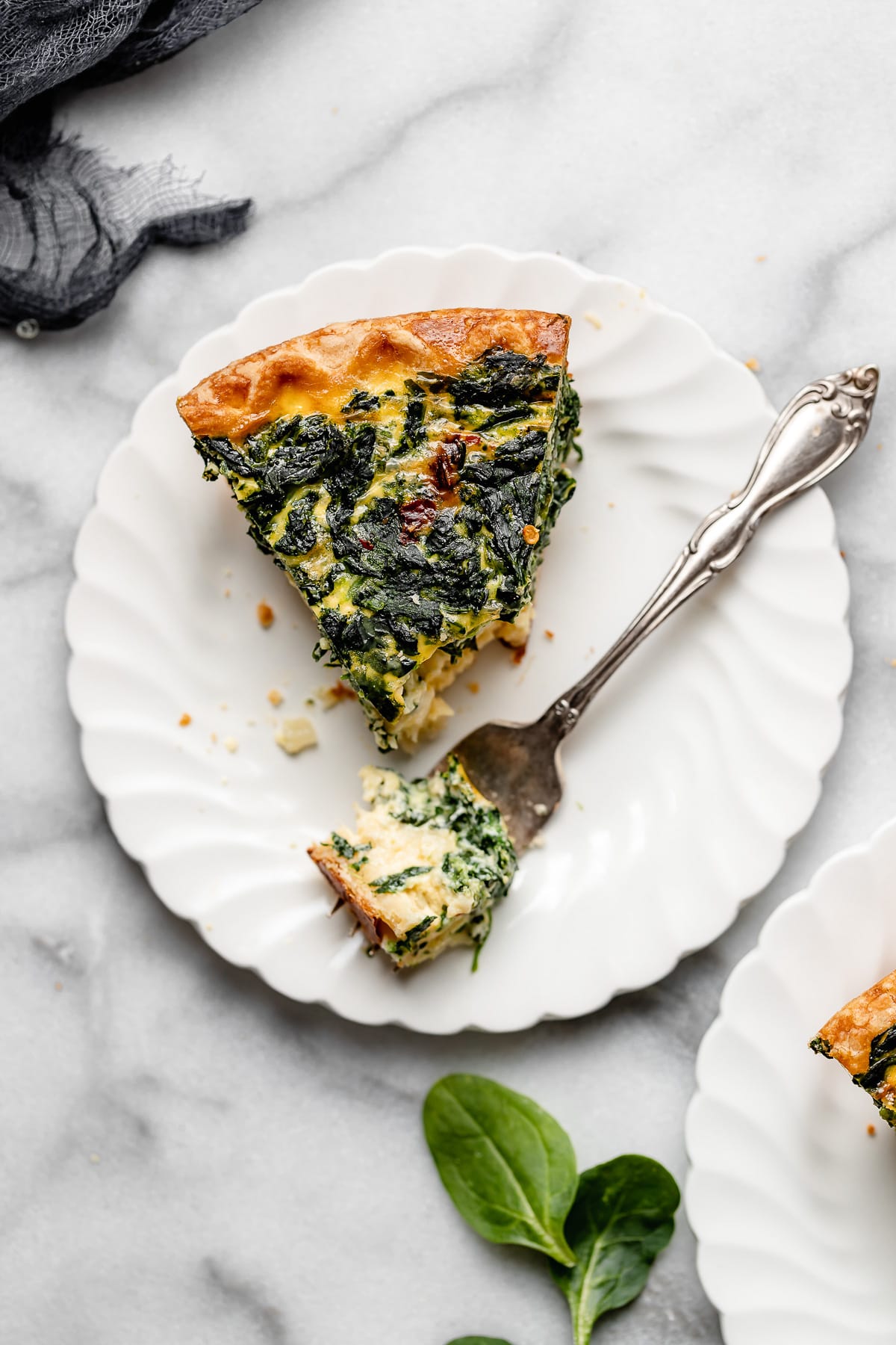 piece of spinach quiche on plate with bite on fork.
