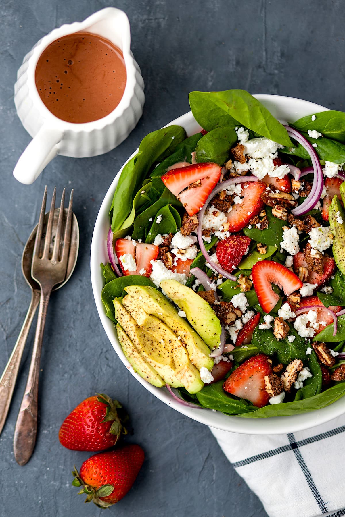 strawberry spinach salad with avocado, candied pecans, feta cheese, and red onion in bowl with strawberry balsamic dressing on the side. 