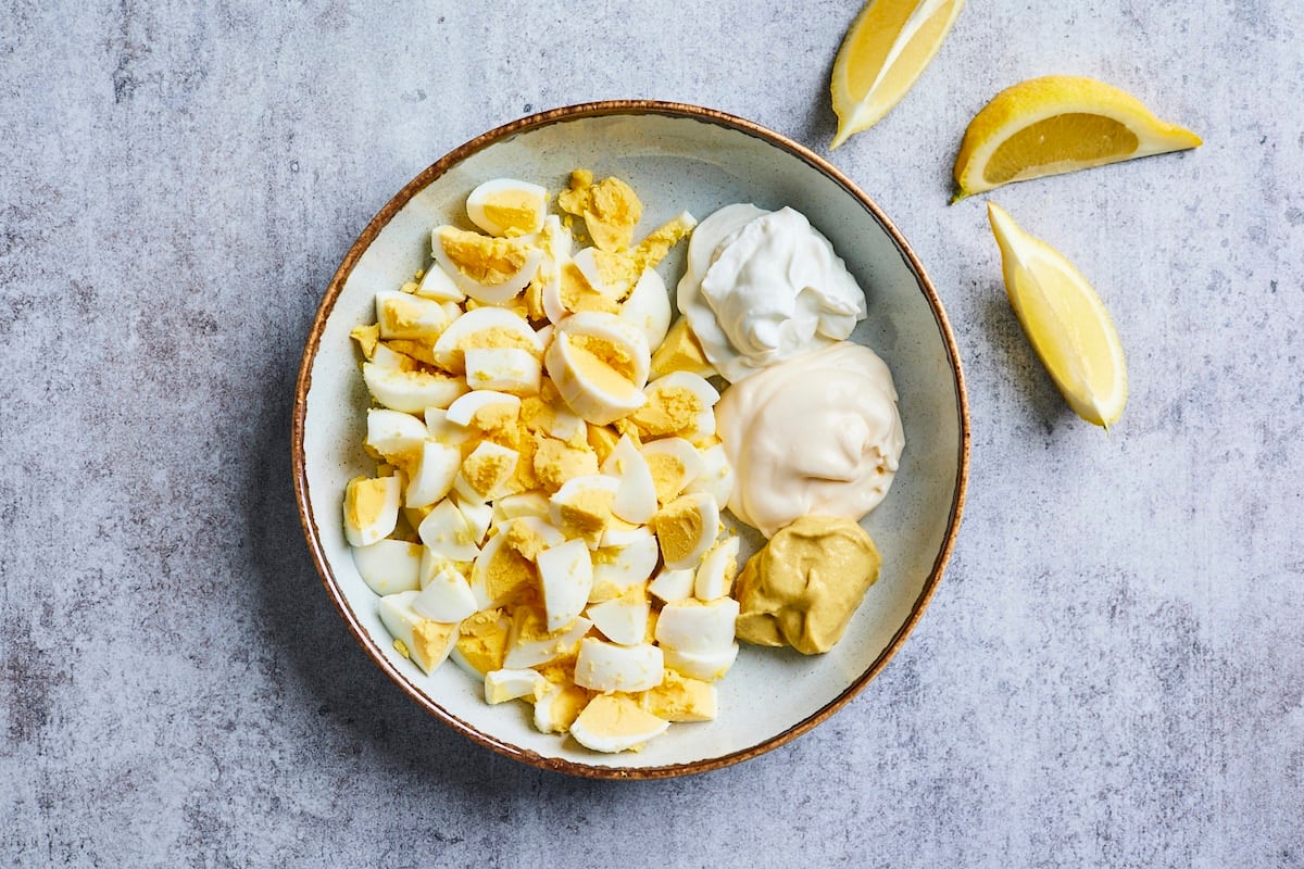 chopped hard boiled eggs in bowl with Greek yogurt, mayonnaise, and Dijon mustard. 