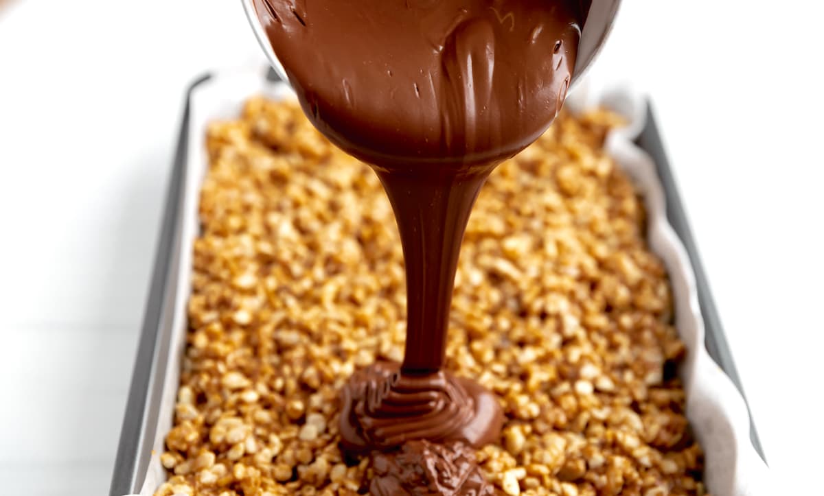 chocolate being poured over scotcheroos in pan. 