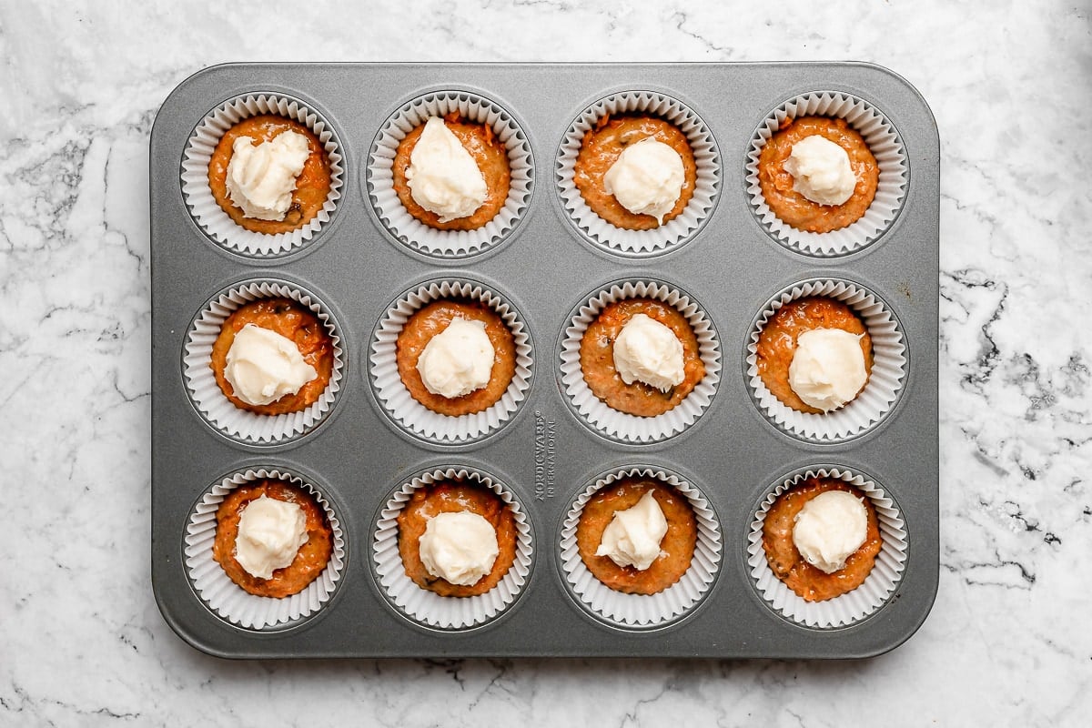 carrot cake muffin batter with cream cheese filling in muffin pan. 