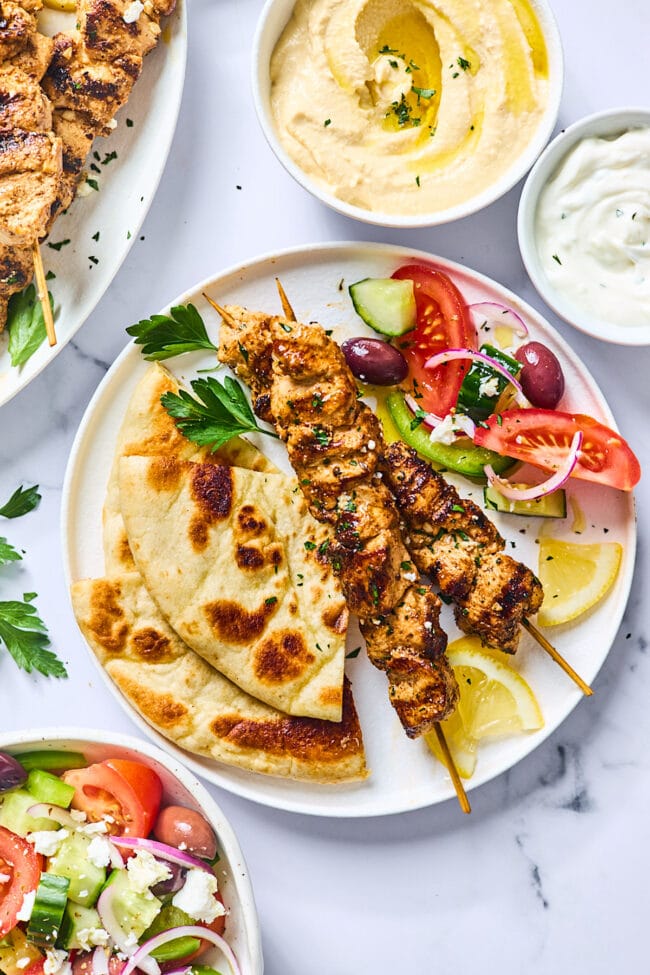 Greek chicken kabobs on plate with pita and Greek salad