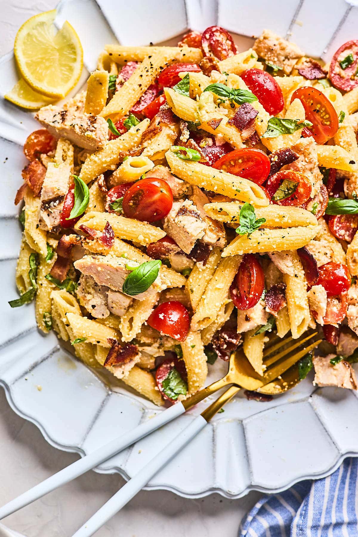 chicken pasta salad with tomatoes and basil on plate with gold silverware. 