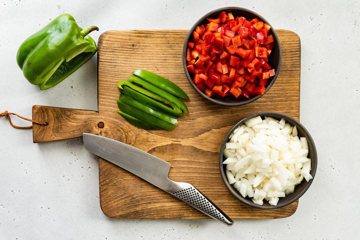 peppers and onion on cutting board with knife to make stuffed pepper soup.