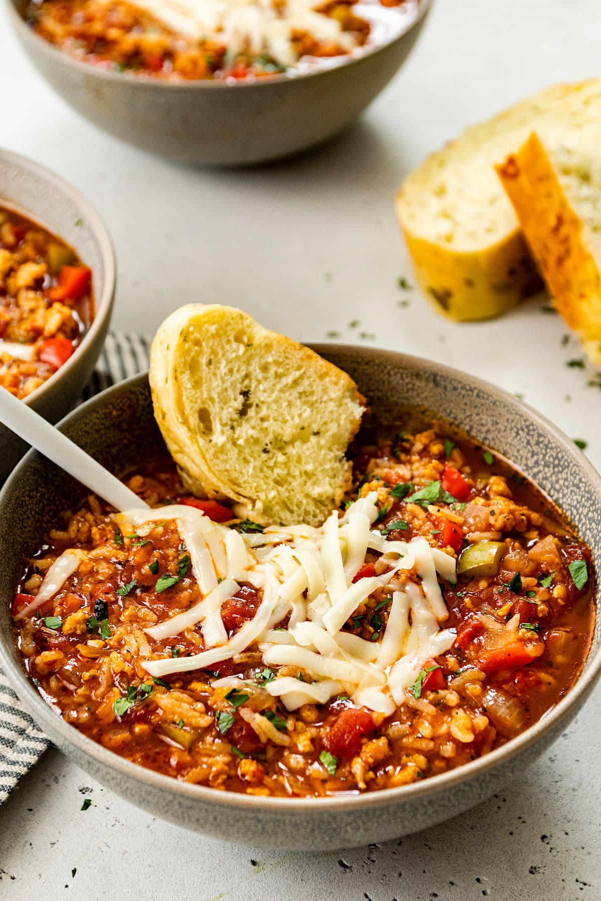 Stuffed pepper soup recipe with shredded cheese and bread in bowl with spoon. 