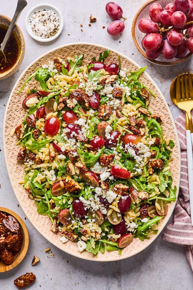 orzo salad with grapes, arugula, feta cheese, and candied pecans on platter.
