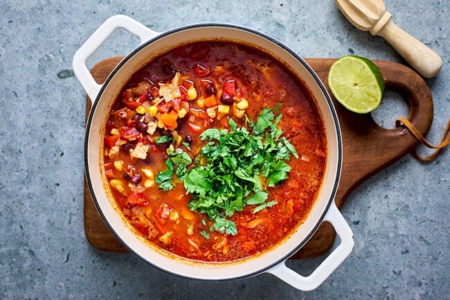 chicken tortilla soup in white pot on wood board with a lime.