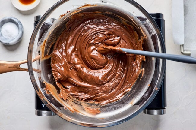 melted fudge in glass bowl over a pan on stove top with a spatula. 