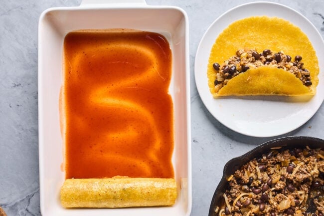rolling beef enchiladas in pan with enchilada sauce