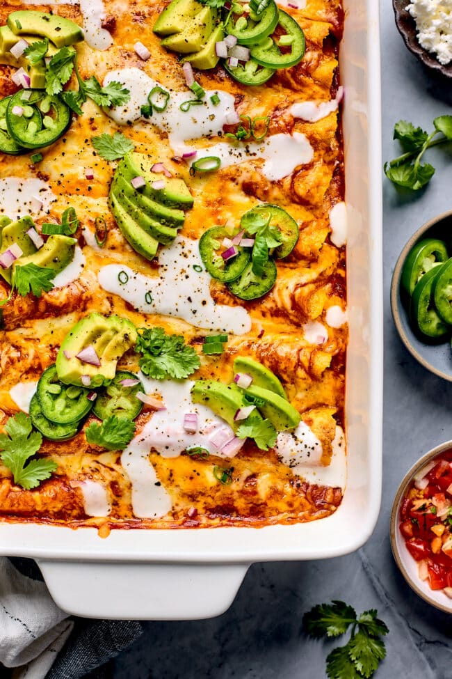 beef enchiladas in pan topped with cheese, avocado, jalapeño, and cilantro 