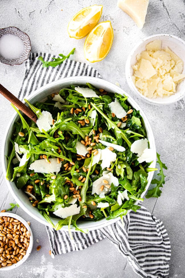 arugula salad in bowl with shaved Parmesan cheese and pine nuts