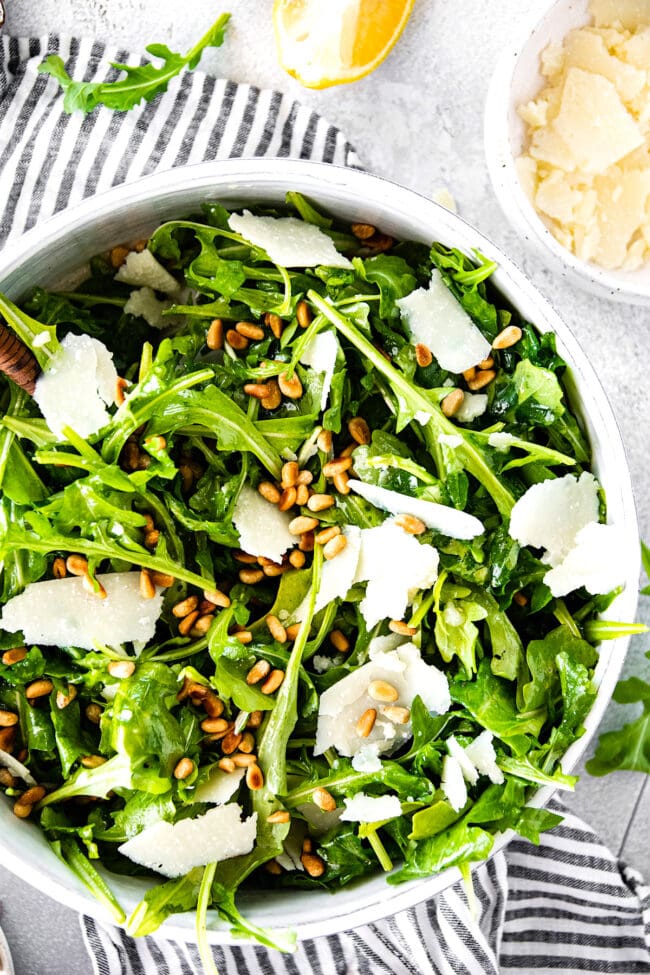 arugula salad in bowl with Parmesan cheese and pine nuts