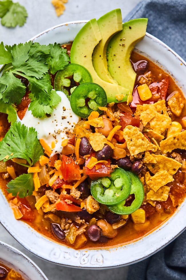 taco soup in a bowl with tortilla chips, sour cream, jalapeño, cilantro, and avocado.