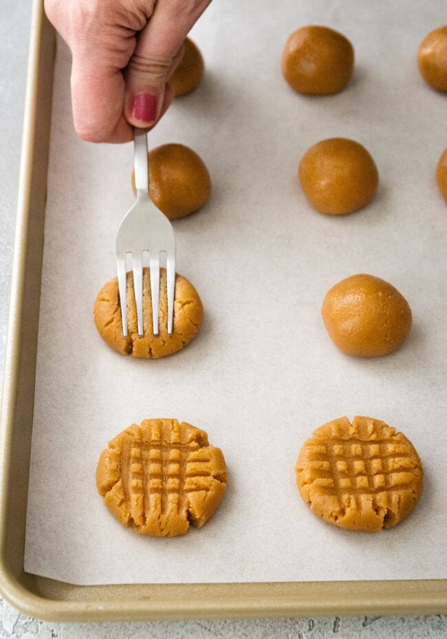 3 ingredient peanut butter cookie dough balls on baking sheet being flattened with a fork