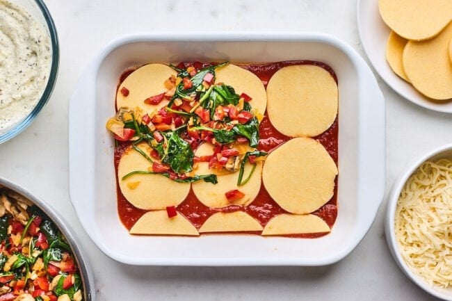 assembling polenta lasagna in pan with sauce, polenta rounds, and vegetables