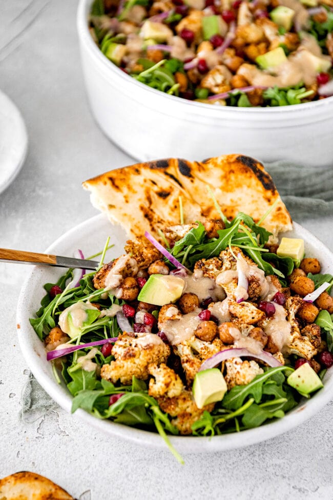 roasted cauliflower chickpea salad with tahini dressing in bowl with pita bread