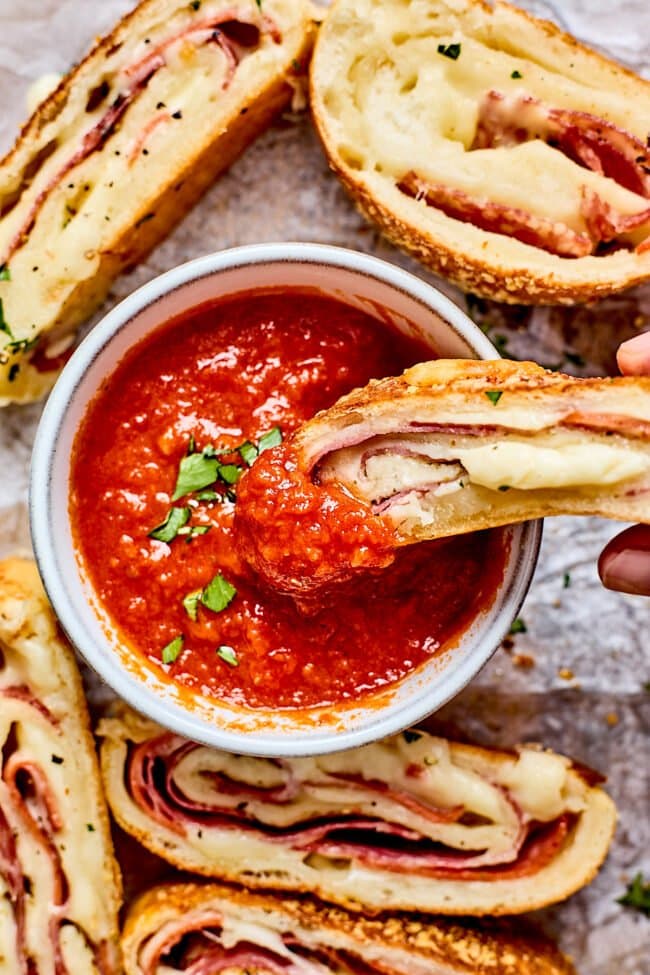 slice of Stromboli dipping into a bowl of marinara sauce