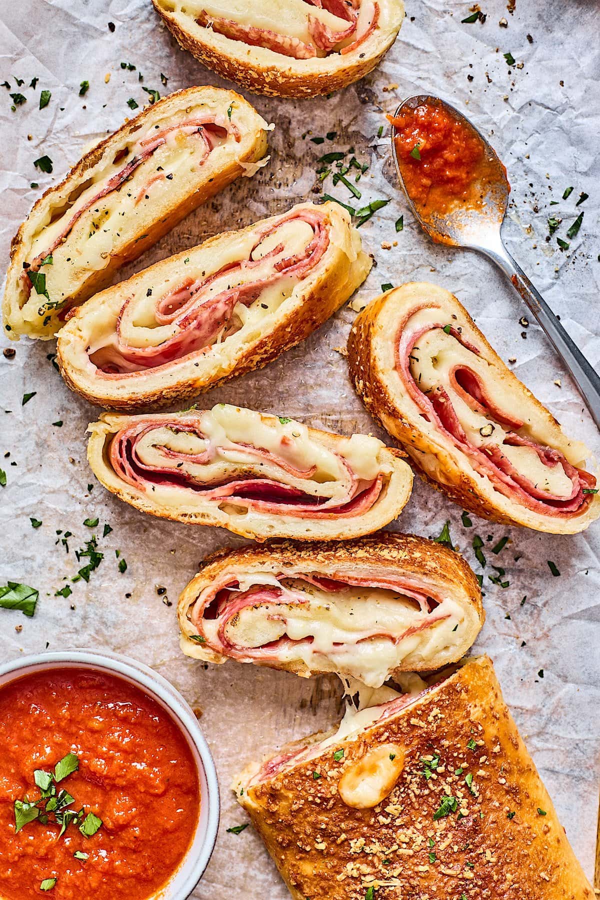 stromboli cut into slices with marinara dipping sauce in bowl on parchment paper. 