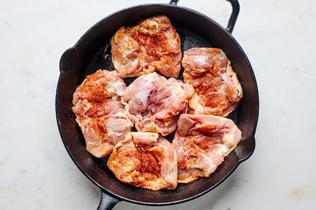 chicken thighs in cast iron skillet with spice rub.