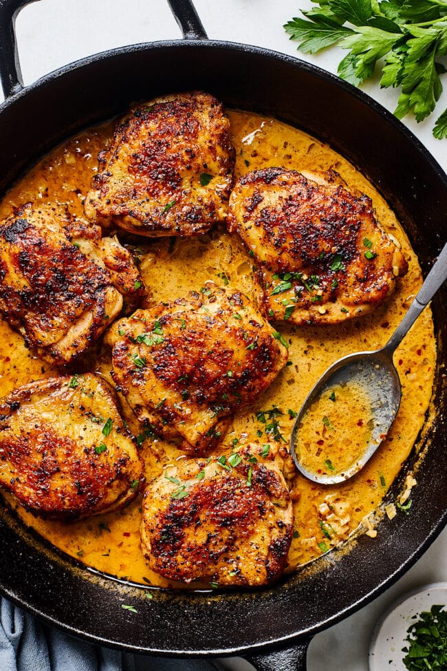 chicken thighs with cream sauce in skillet with spoon.