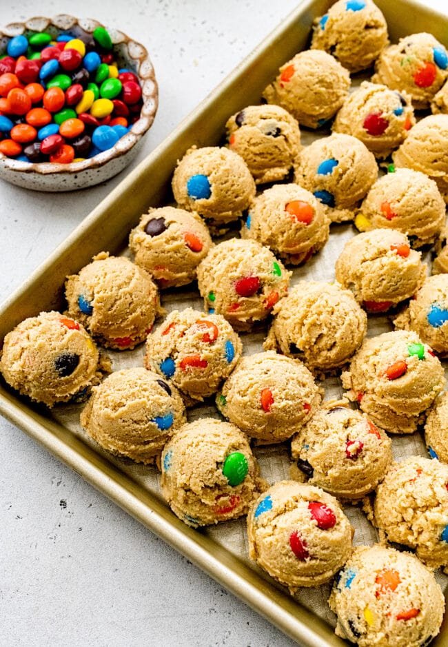 M&M cookie dough balls on baking sheet.