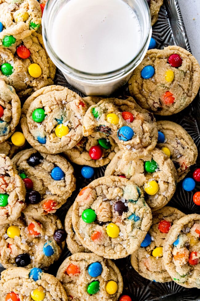 M&M cookies on baking sheet with glass of milk.