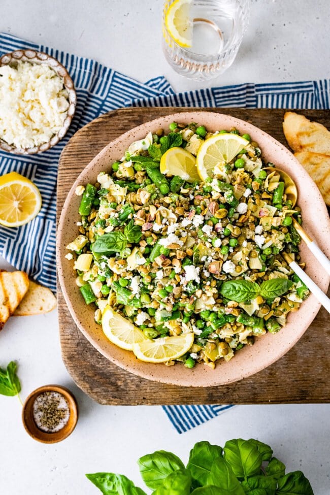 spring lentil salad in bowl with lemon wedges.