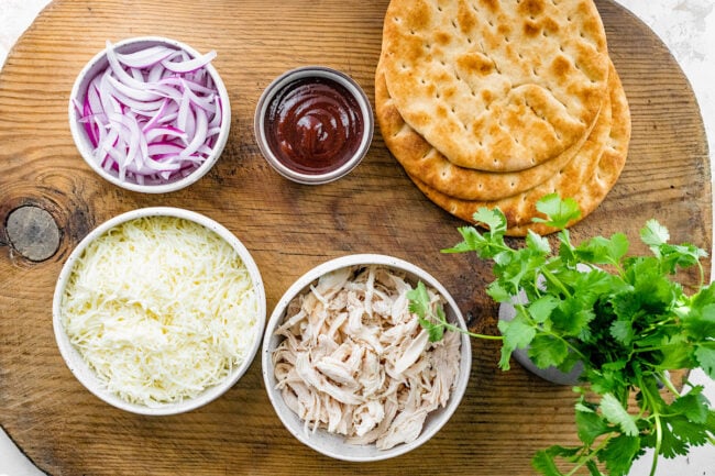 BBQ chicken pita pizza ingredients on cutting board.