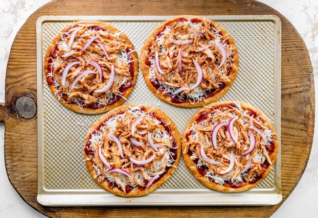 BBQ chicken pita pizzas unbaked on baking sheet. 