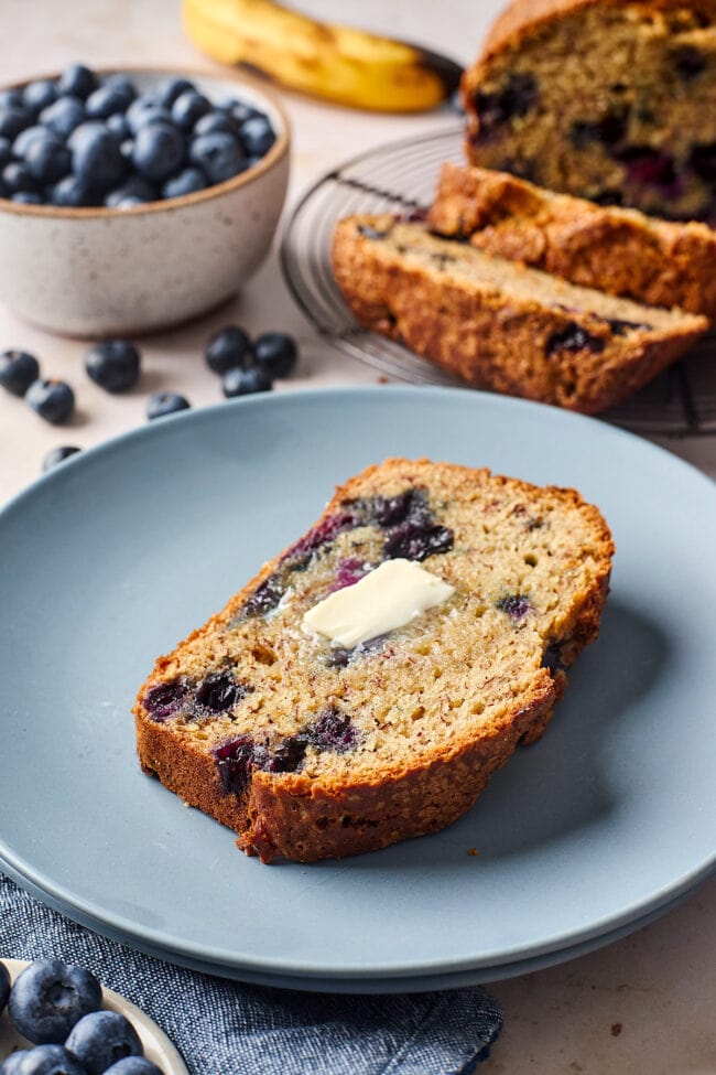 slice of blueberry banana bread on plate with butter.