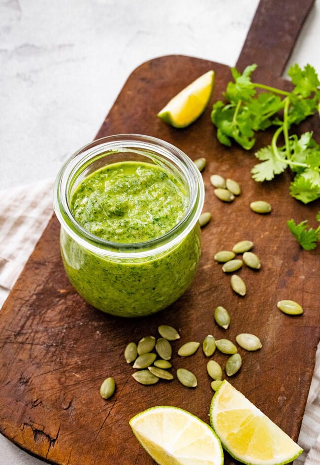 cilantro pesto in jar with pepitas and lemon wedges. 