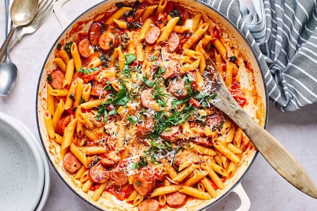 sausage pasta in pot with parmesan cheese, basil, and wooden spoon.