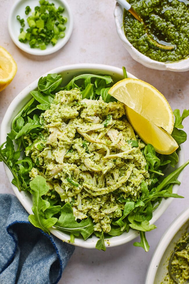 pesto chicken salad on greens with lemon wedges.