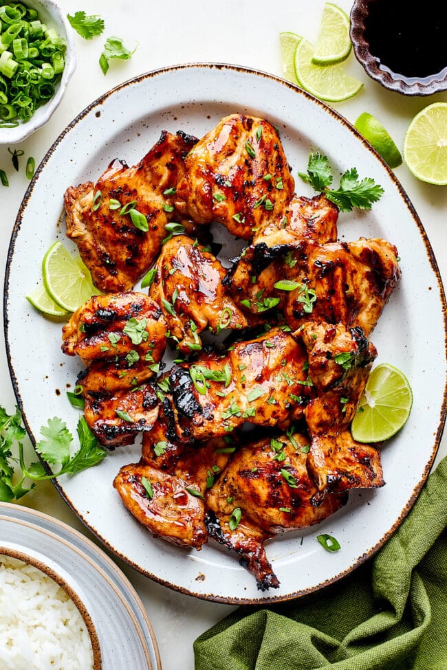 Soy ginger chicken on platter with lime wedges and green onion. 