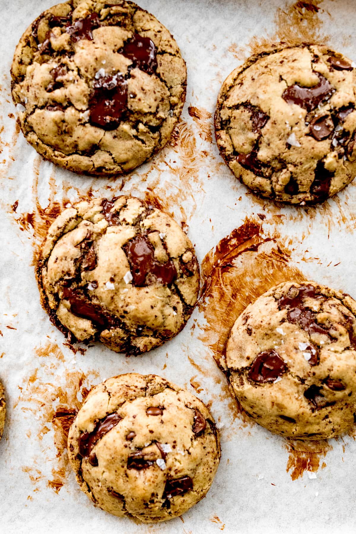 chocolate chip cookies with flaky sea salt on baking sheet with parchment paper. 