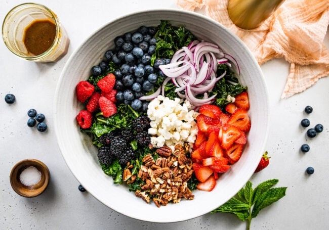 kale salad with berries, pecans, feta cheese, and red onions in a bowl. 