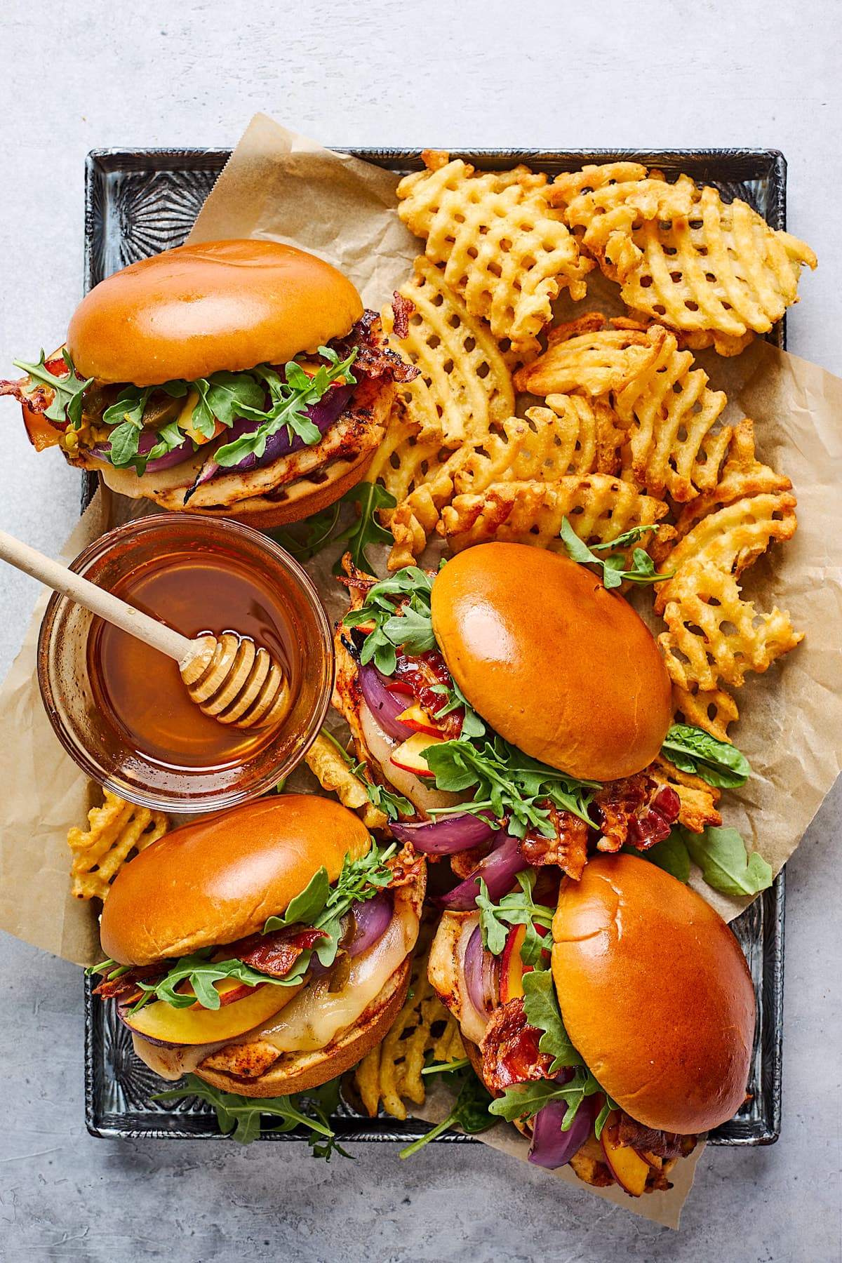 grilled chicken sandwiches with waffle fries and jar of hot honey in pan. 