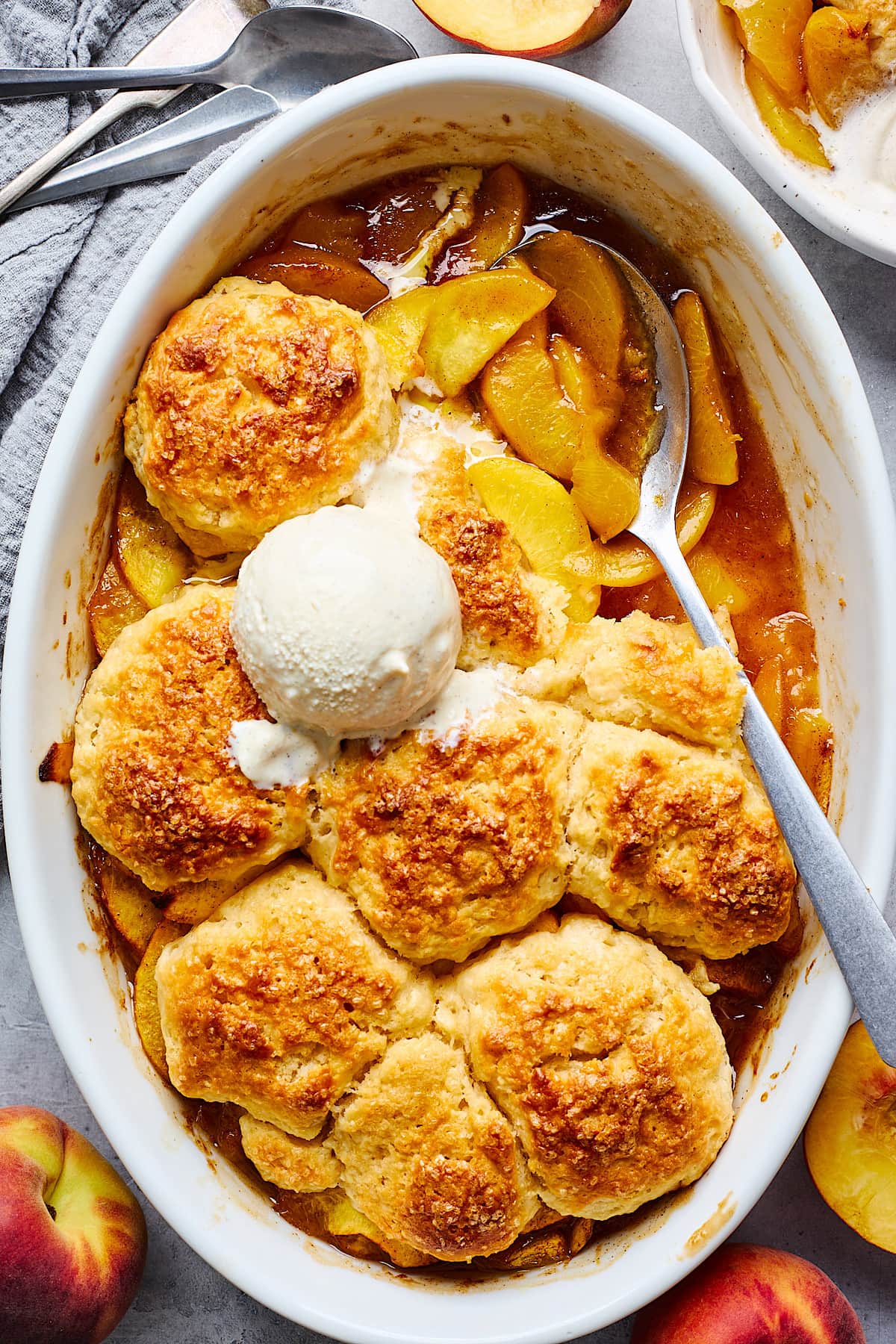 peach cobbler in baking dish with spoon and vanilla ice cream.