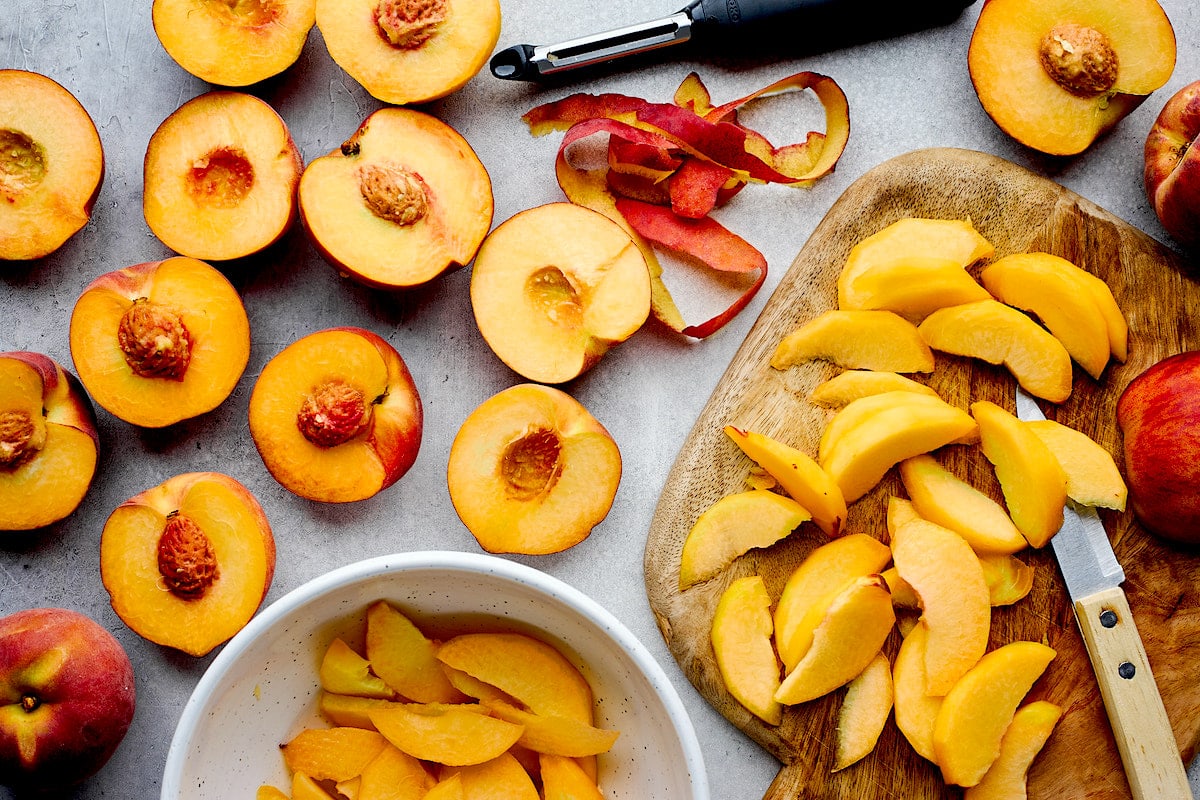 peaches and peach slices on cutting board with knife and peeler. 