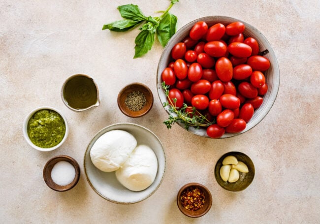 tomatoes, burrata cheese, pesto, garlic, and olive oil in bowls. 