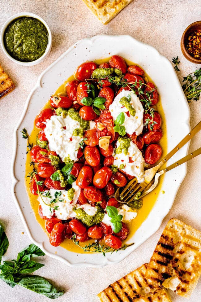 roasted tomatoes on platter with burrata cheese, pesto, garlic, and olive oil. 