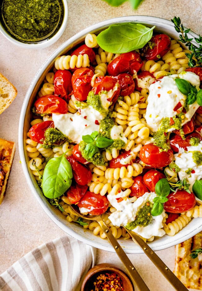 roasted tomatoes with burrata in bowl with pasta, pesto, and herbs.