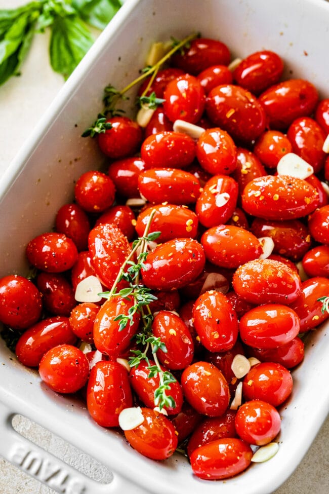 grape tomatoes with olive oil, herbs, and garlic in baking dish. 