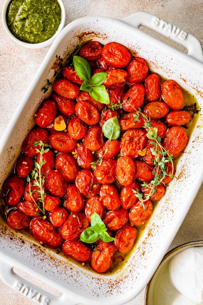 roasted tomatoes in baking dish with fresh herbs.