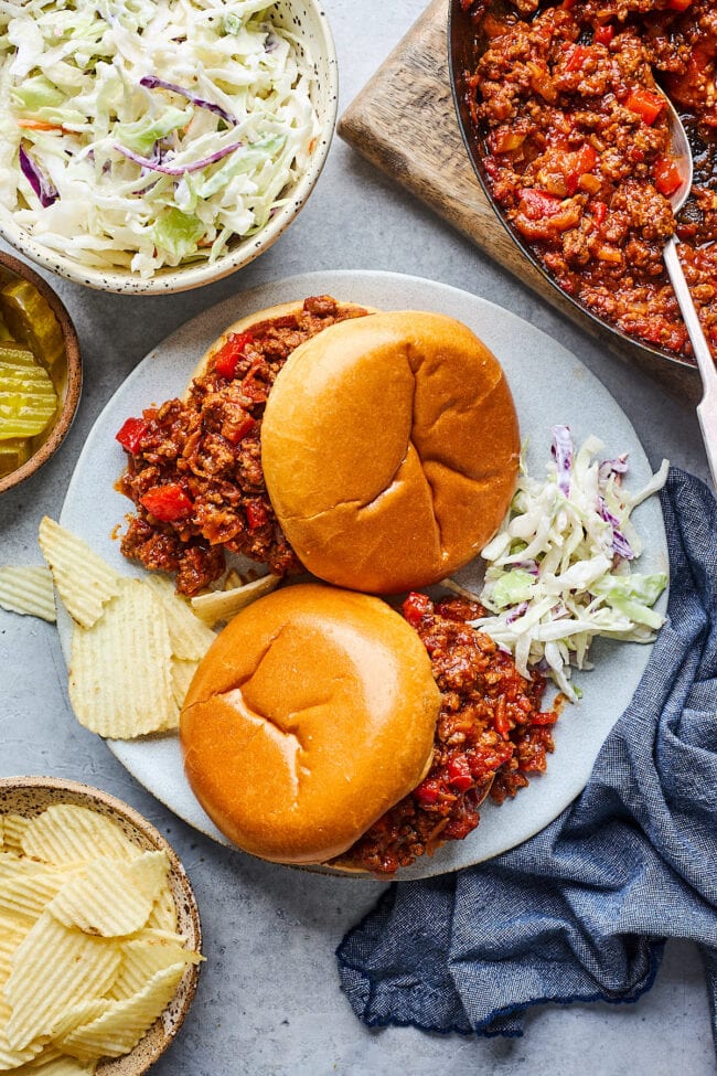 sloppy joes on plate with potato chips and cole slaw. 
