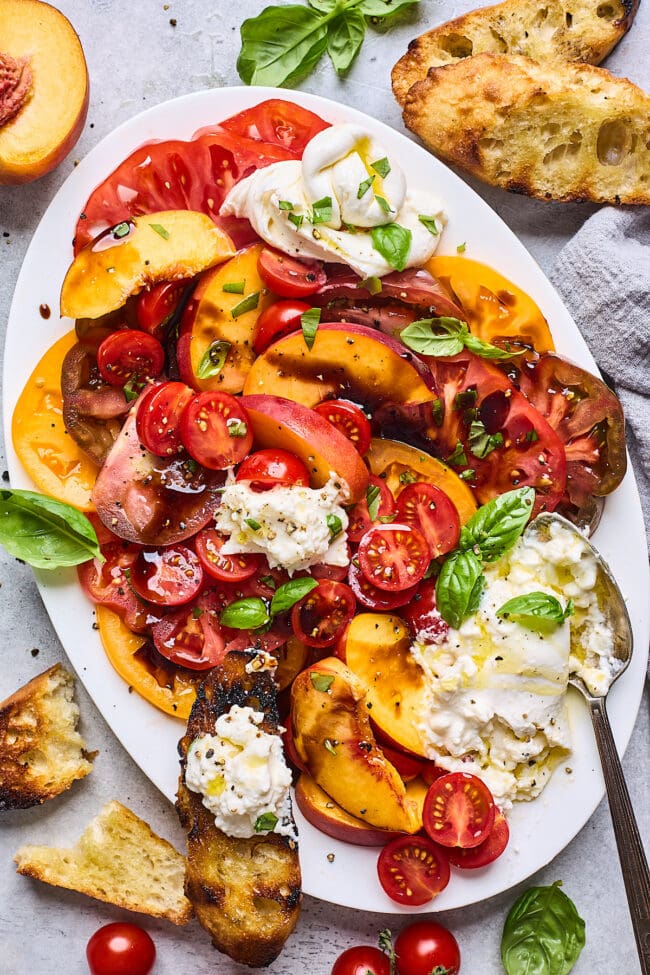tomato peach burrata salad on plate with grilled bread and basil. 