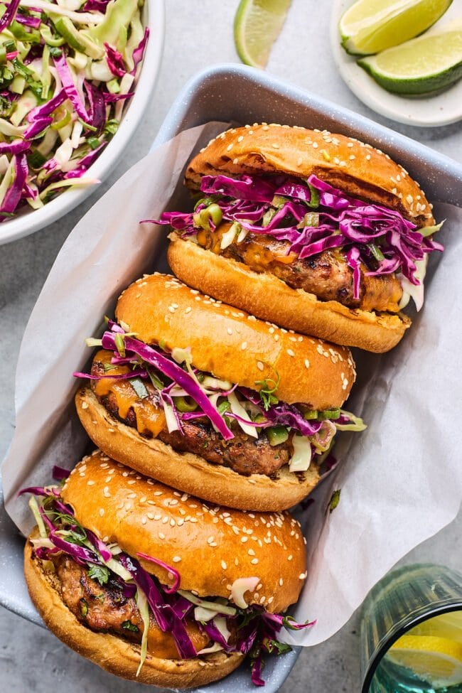 turkey burgers on buns with slaw in pan with parchment paper.