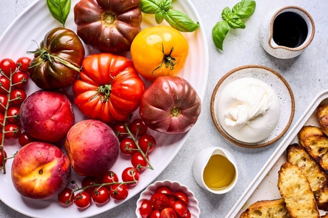 tomatoes and peaches on plate with burrata cheese, olive oil, balsamic glaze, and bread.