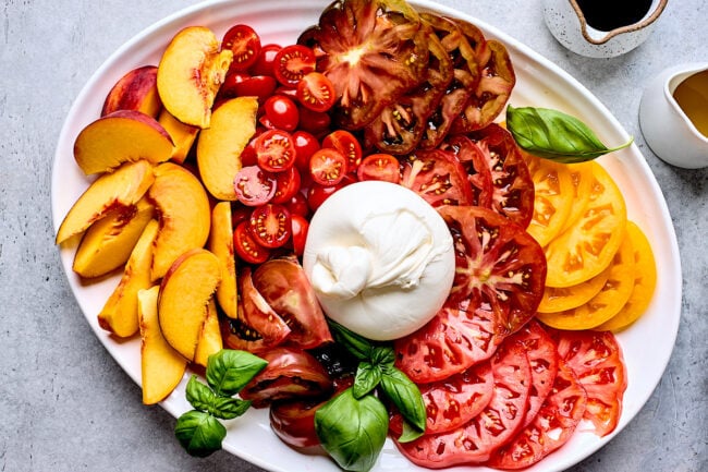 peaches, tomatoes, burrata cheese, and basil on platter.